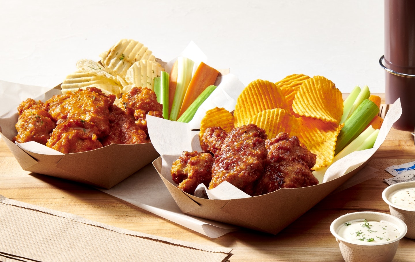 Two types of sauced wings with chips and vegetables in cardboard boats