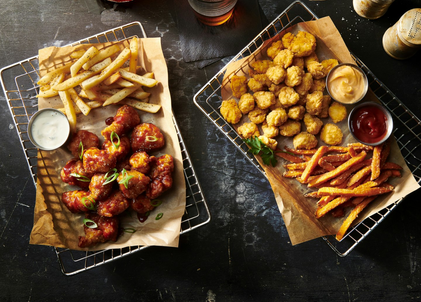 Popcorn chicken and boneless sauced wings with fries in wire baskets